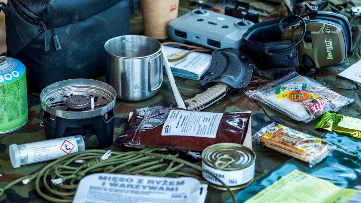 A diverse assortment of camping and survival items laid out, including food, tools, and gadgets.